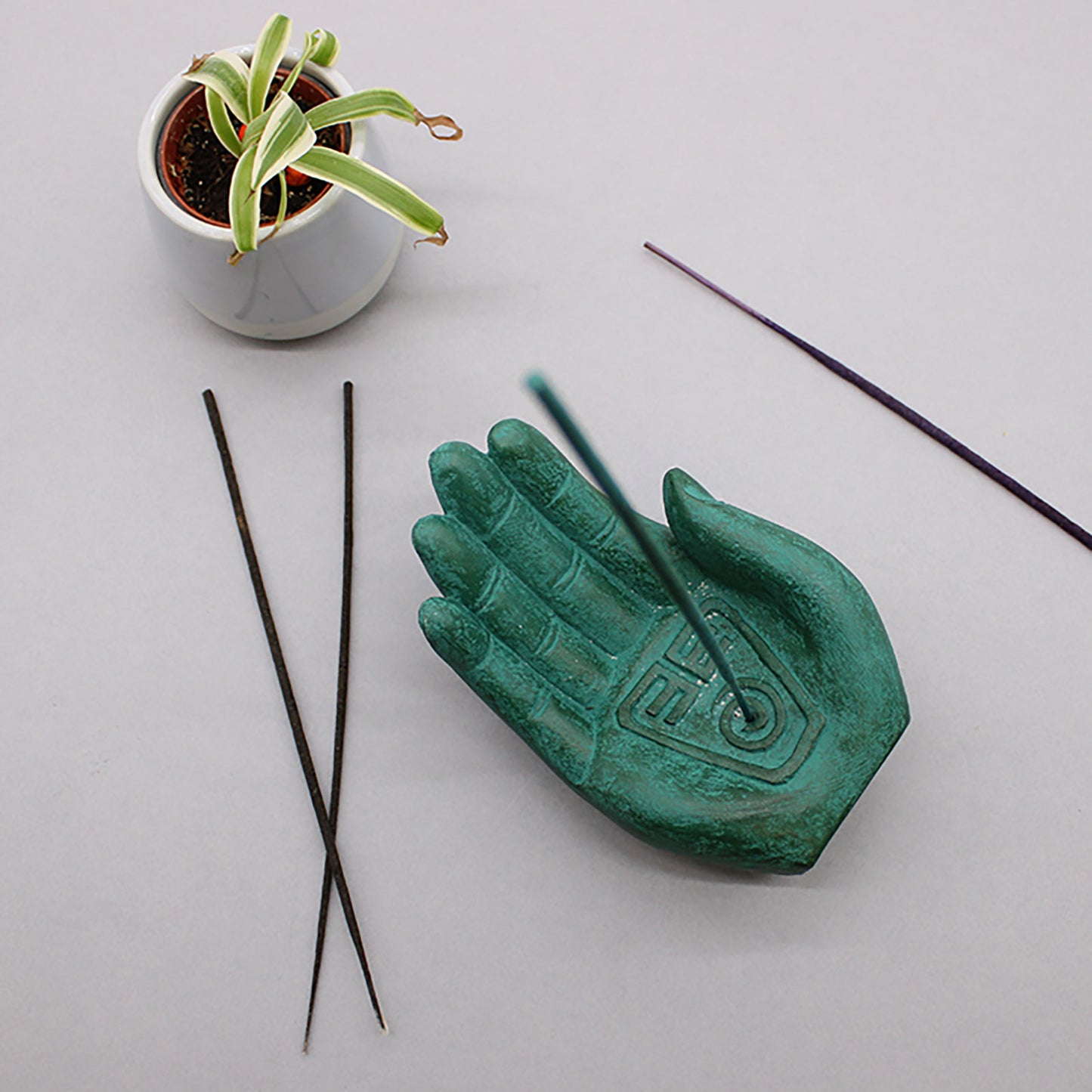 Green hand-shaped incense burner with incense stick with white background
