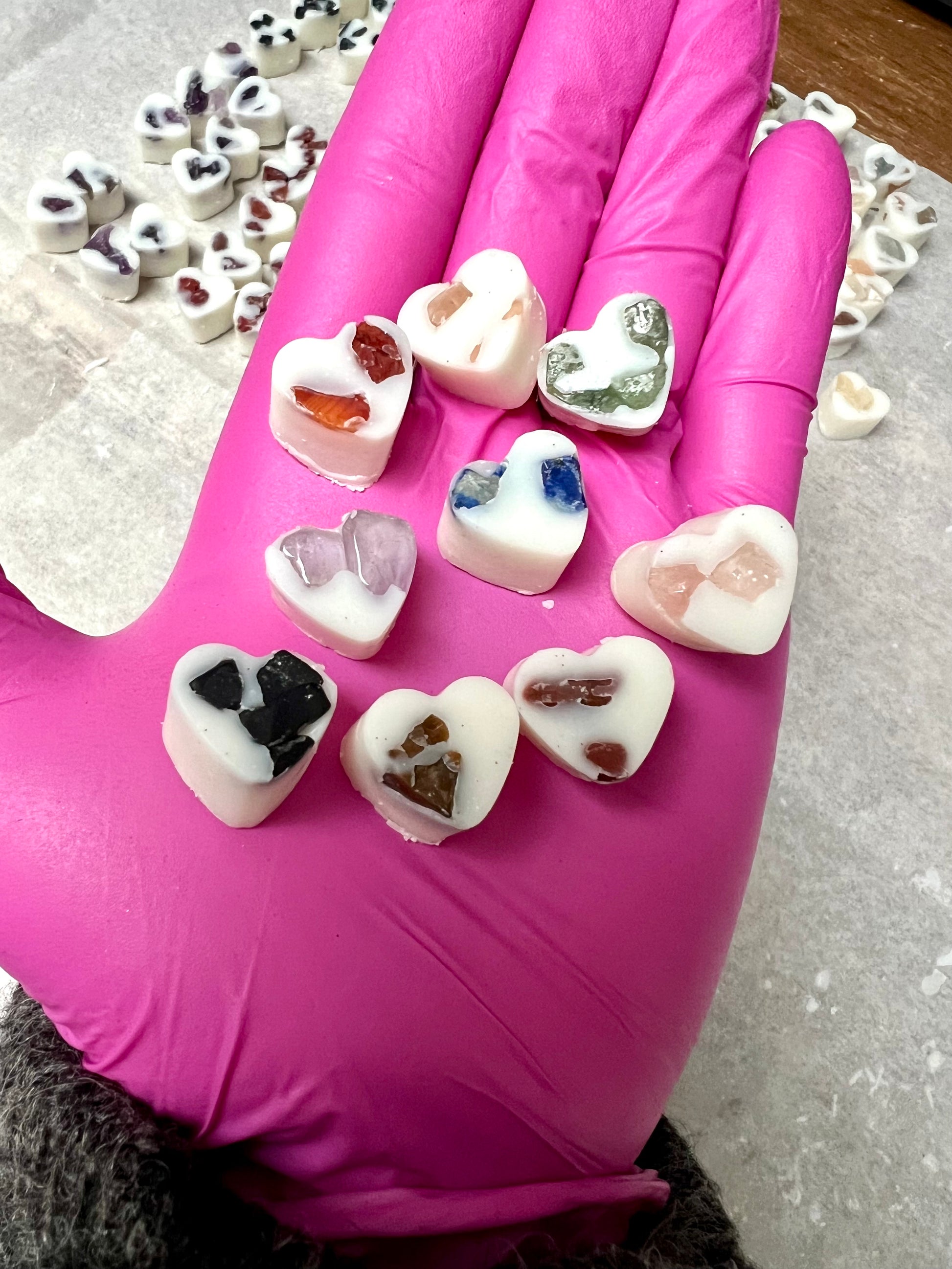 Heart-shaped soy wax melts with embedded crystal stones held in a pink glove.