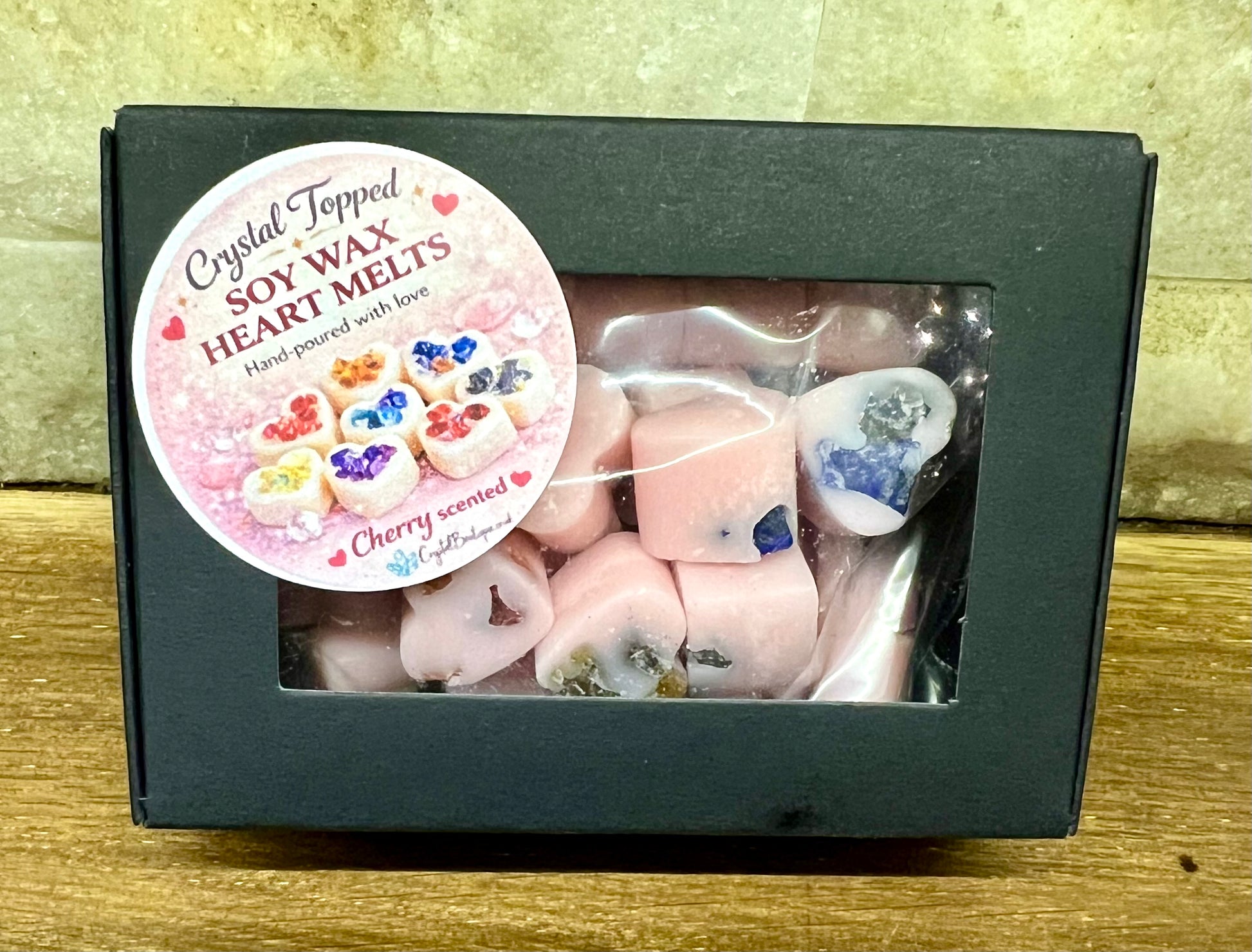 Box of crystal-topped soy wax heart melts with a decorative label on a wooden surface - cherry fragranced.