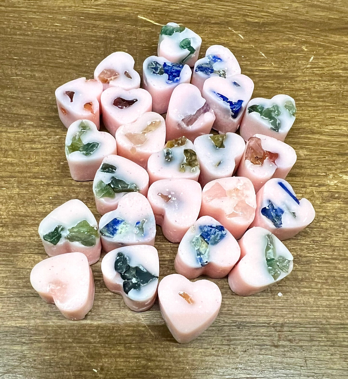 Heart-shaped soy wax melts with embedded crystal chips on a wooden surface