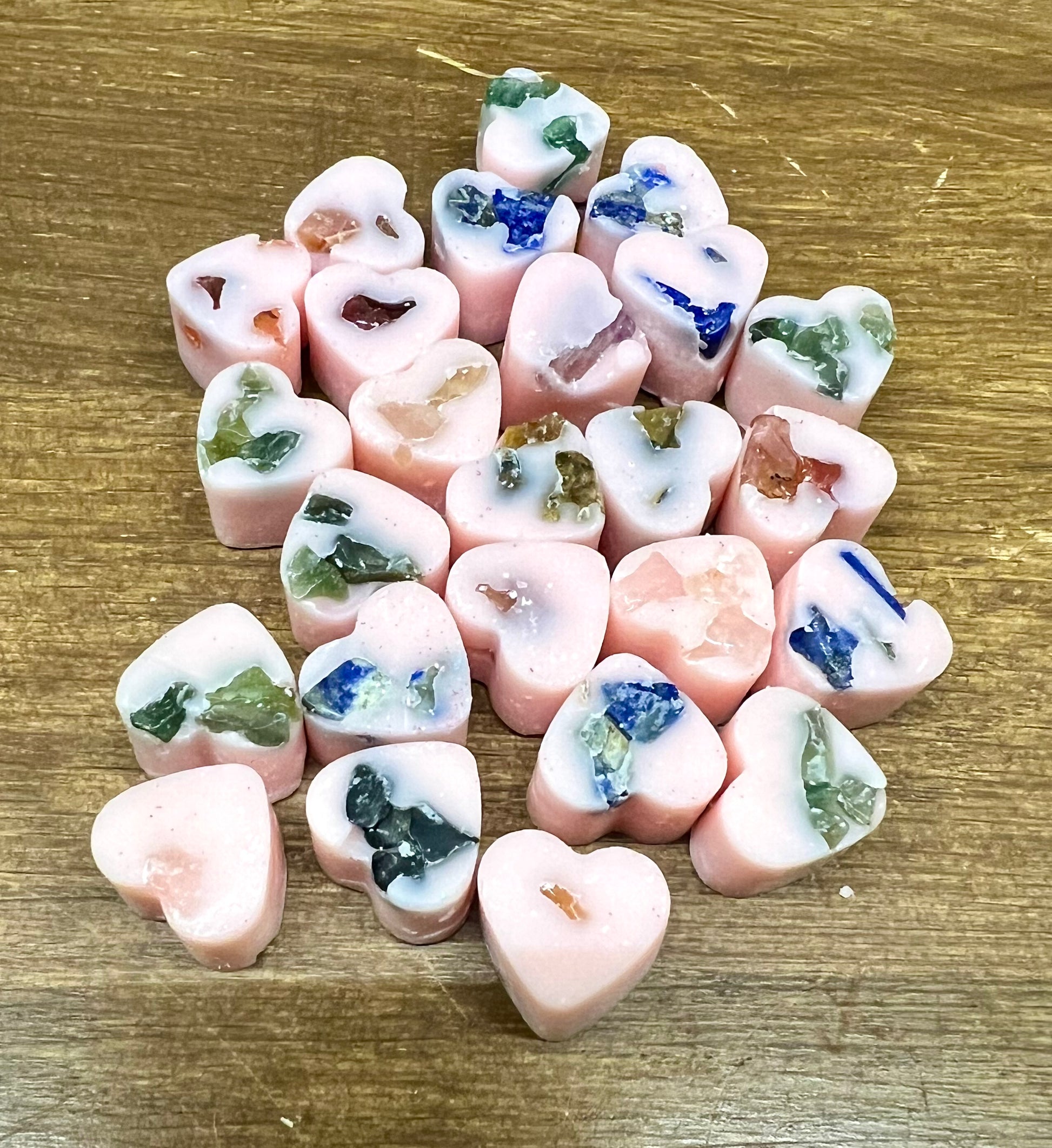 Heart-shaped soy wax melts with embedded crystal chips on a wooden surface