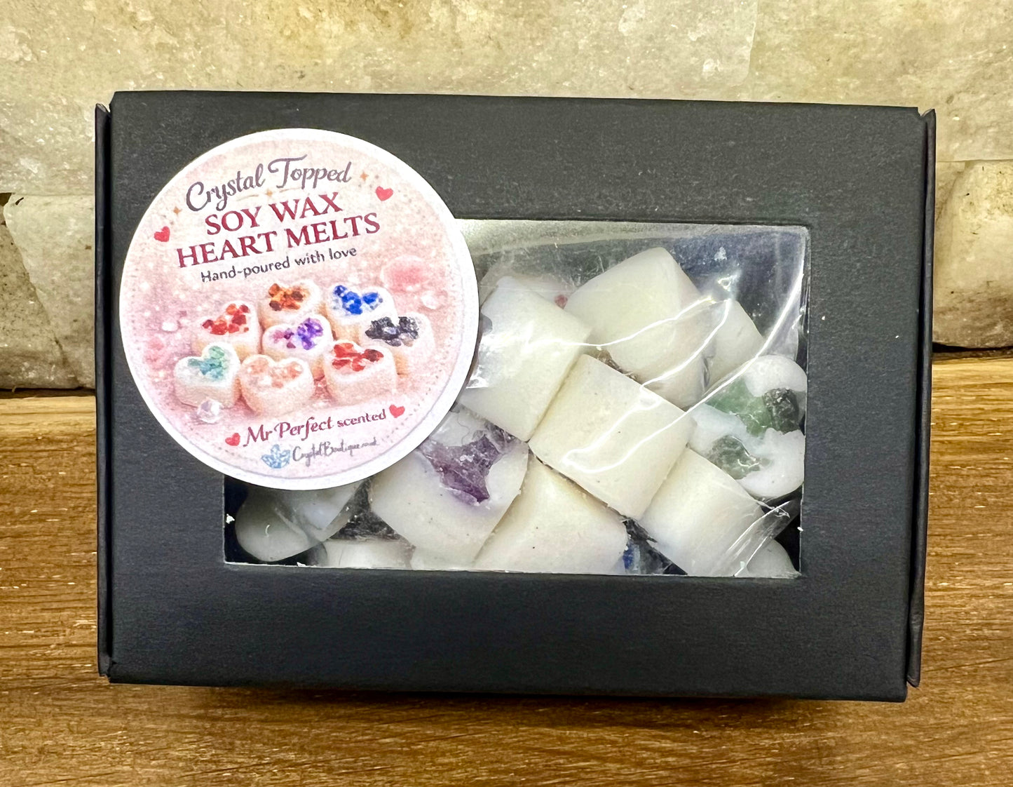 Box of crystal-topped soy wax heart melts with a decorative label on a wooden surface.