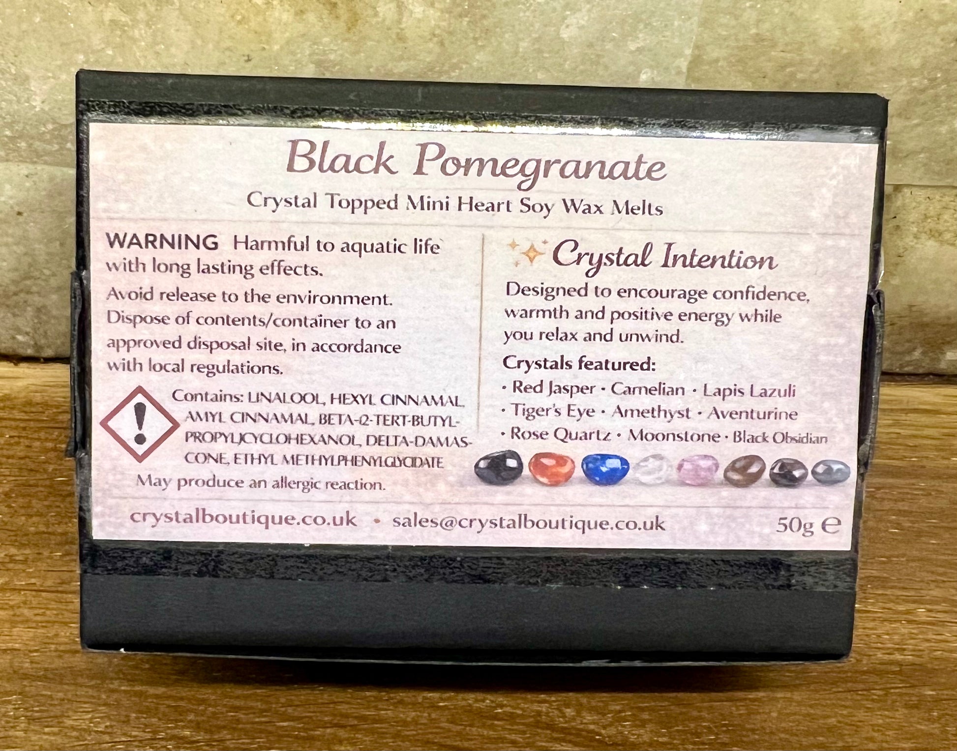 Box of Black Pomegranate crystal-topped soy wax melts with warning label and crystal list on a wooden surface.