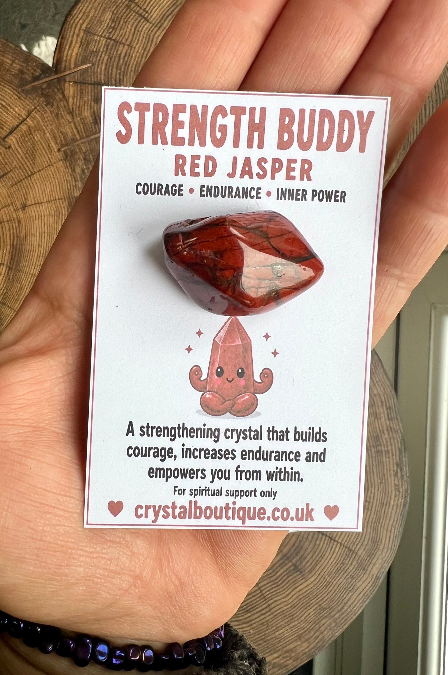 Card with red jasper stone and 'Strength Buddy' text held by a hand.