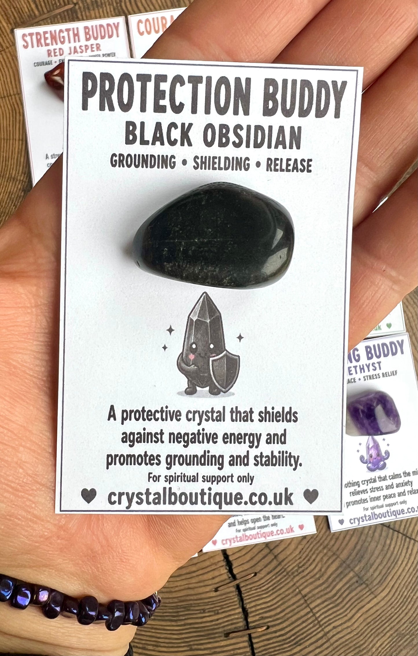Black Obsidian crystal with packaging labeled 'Protection Buddy' held by a hand.