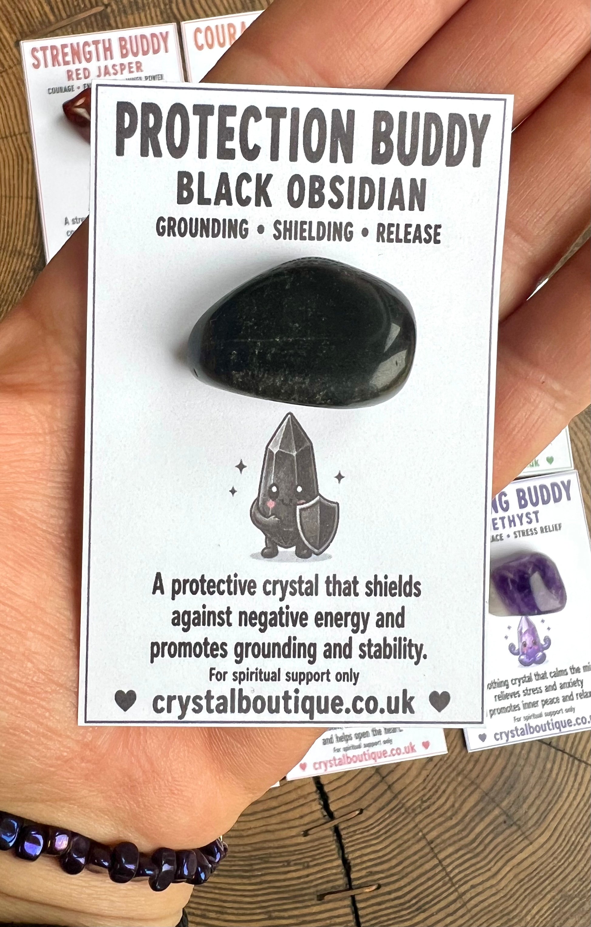 Black Obsidian crystal with packaging labeled 'Protection Buddy' held by a hand.