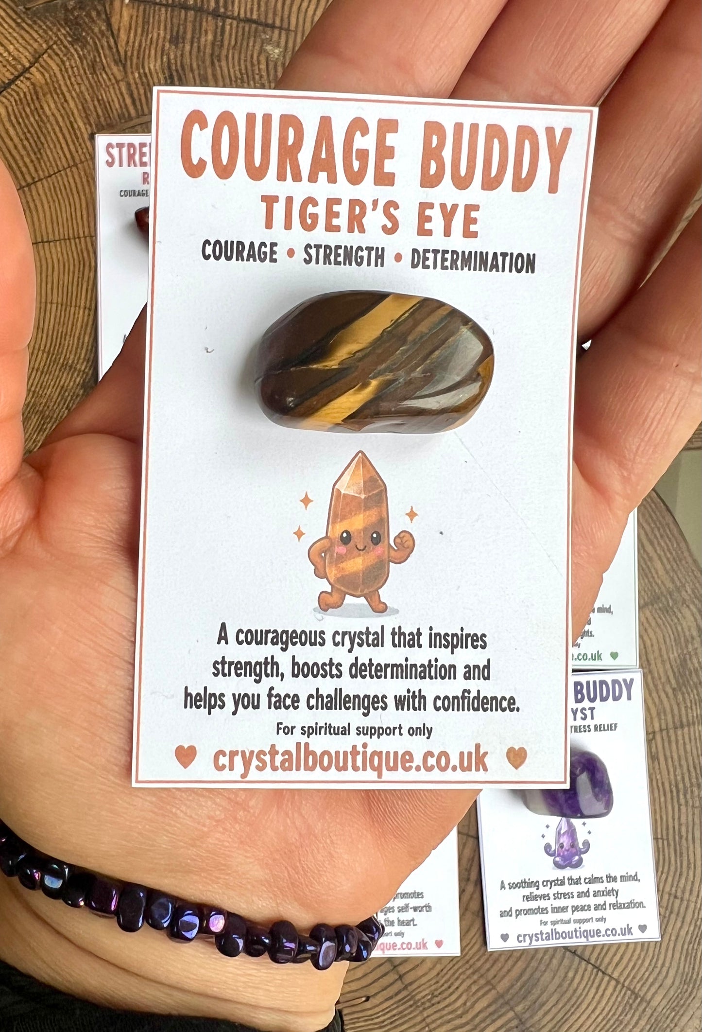Crystal with packaging labeled 'Courage Buddy Tiger's Eye' held by a hand.