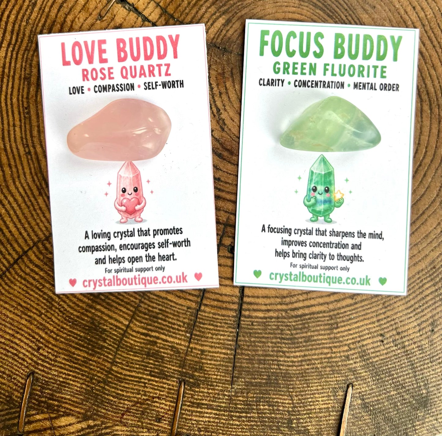 Two crystal cards on a wooden surface, one labeled 'Love Buddy Rose Quartz' and the other 'Focus Buddy Green Fluorite'.