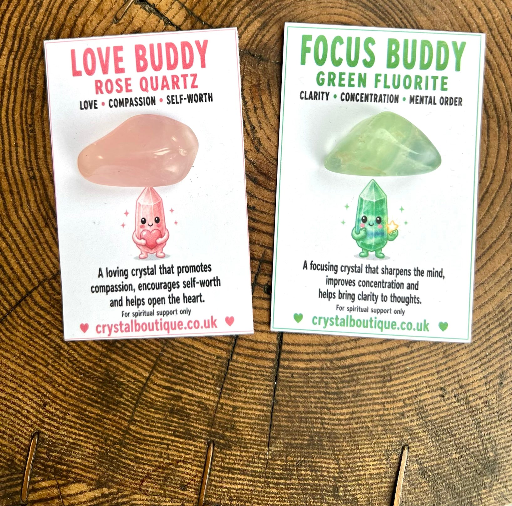 Two crystal cards on a wooden surface, one labeled 'Love Buddy Rose Quartz' and the other 'Focus Buddy Green Fluorite'.