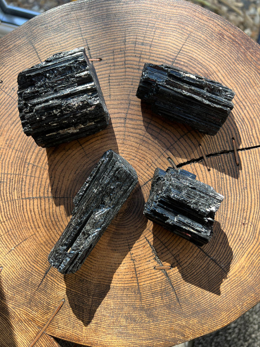 Four dark, textured black Tourmaline mineral stone chunks with a layered, crystalline structure, arranged on a rustic wooden log slice.