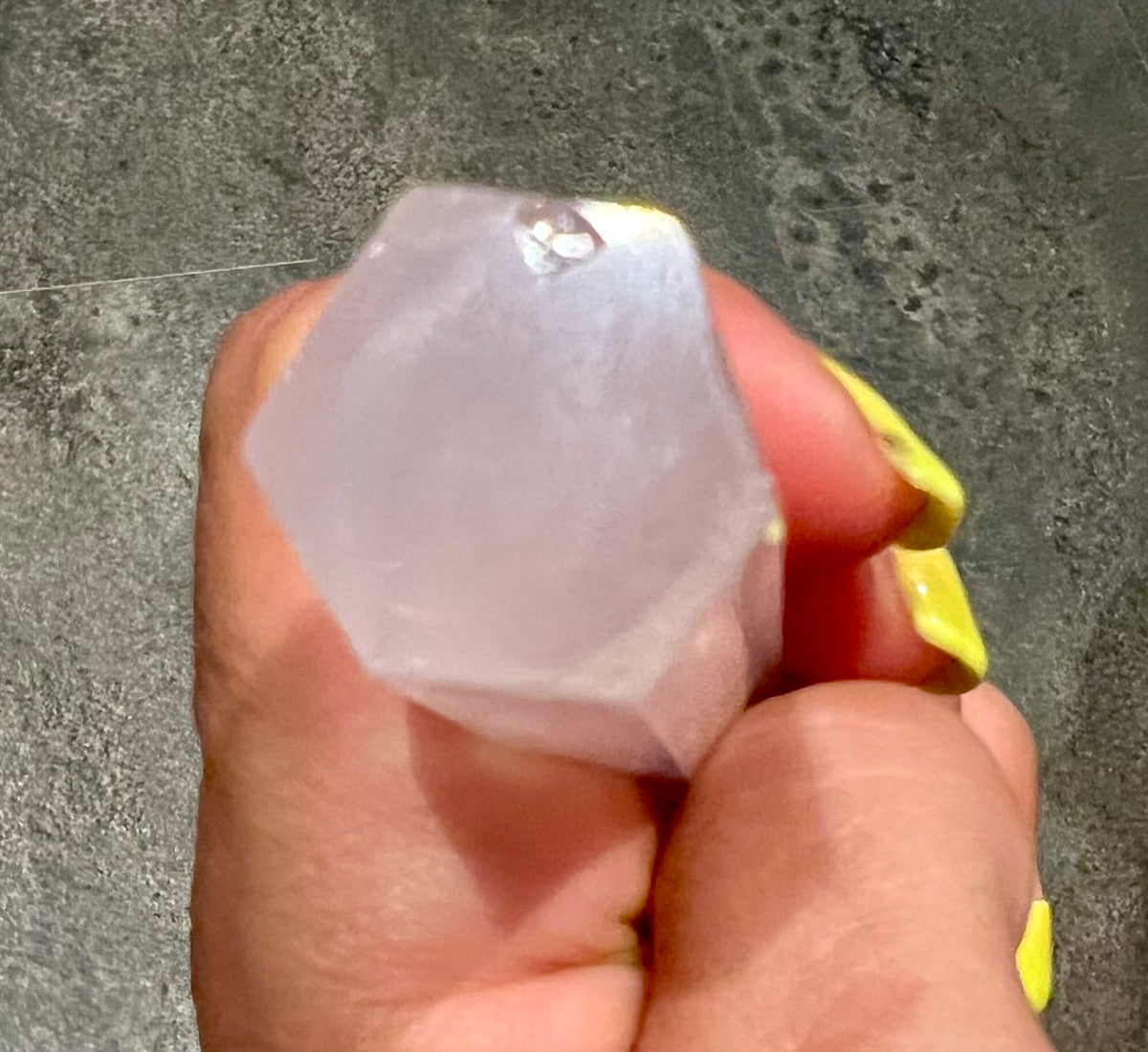 A hand holds a faceted underside of, a  pale pink rose quartz crystal gemstone against a gray textured background.