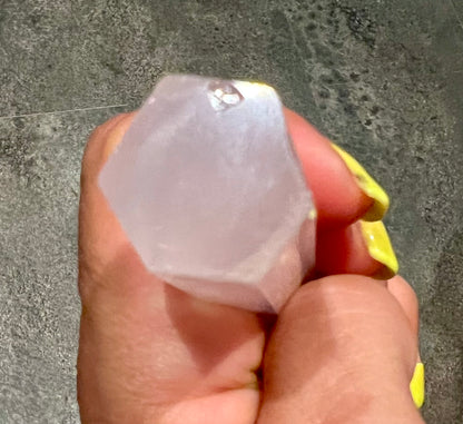 A hand holds a faceted underside of, a  pale pink rose quartz crystal gemstone against a gray textured background.