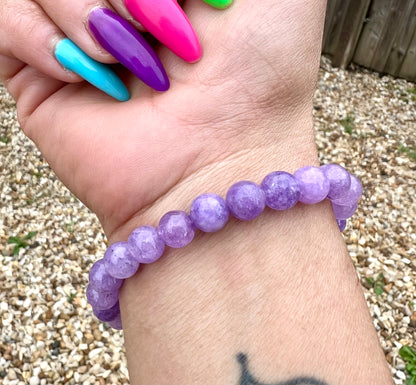 Hand wearing a purple Amethyst lavender beaded bracelet with colorful nails in the background.