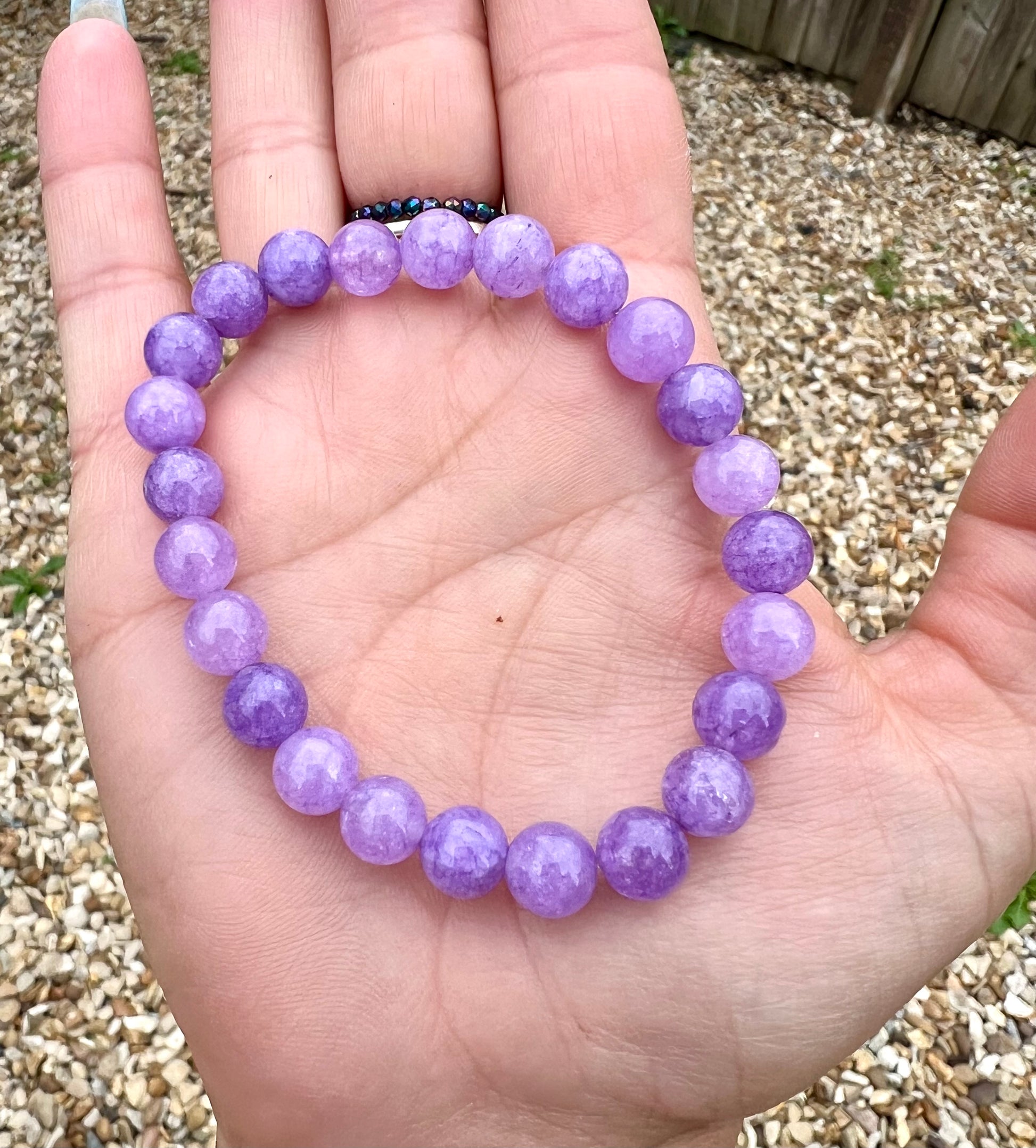 Hand wearing a purple Amethyst lavender beaded bracelet with colorful nails in the background.