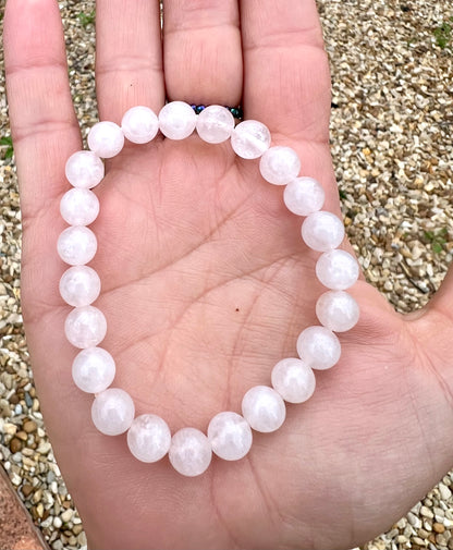 Hand wearing a light pink rose quartz crystal beaded bracelet on a wrist.