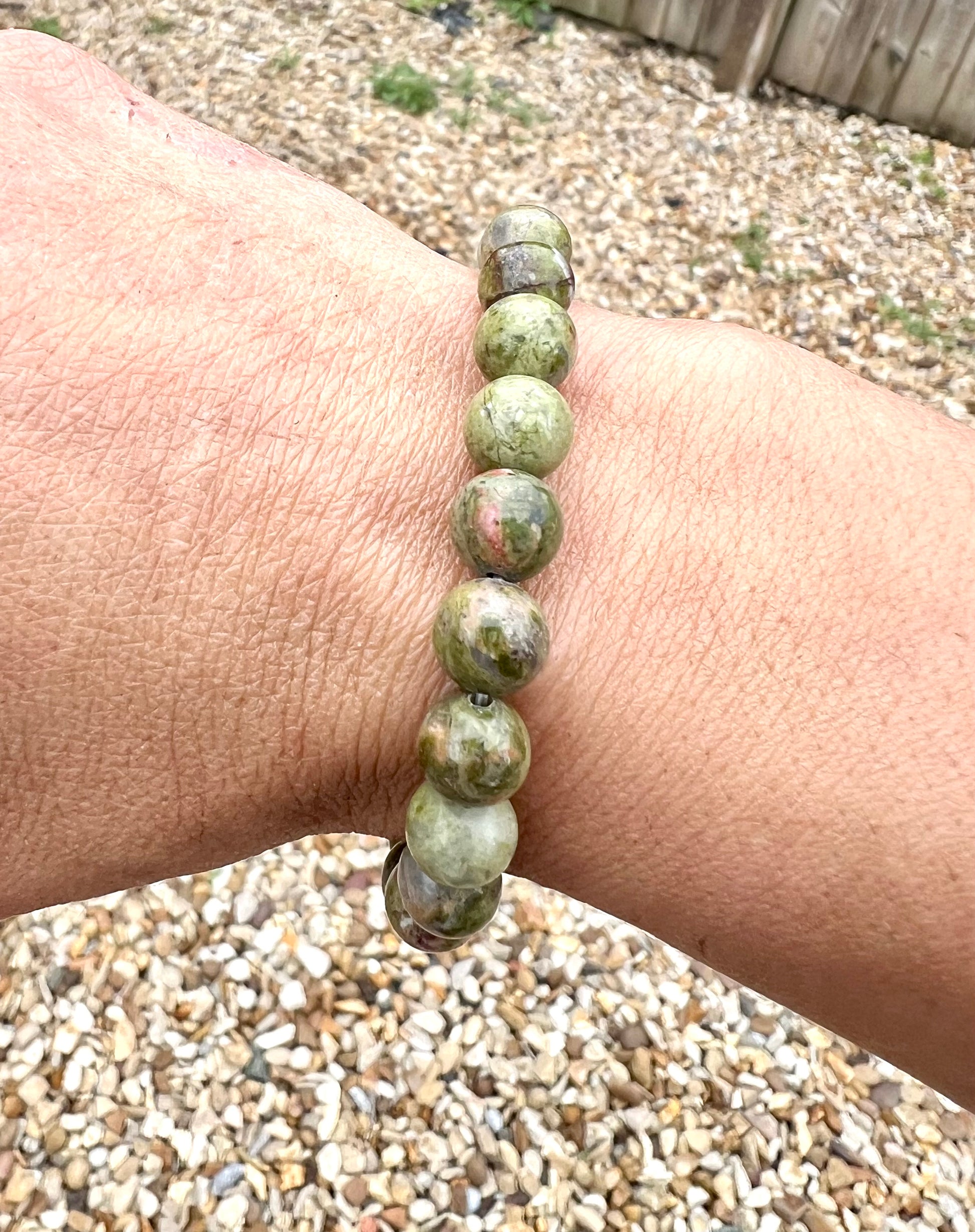 A hand wearing a bracelet composed of 8mm round green Unakite crystal gemstones.