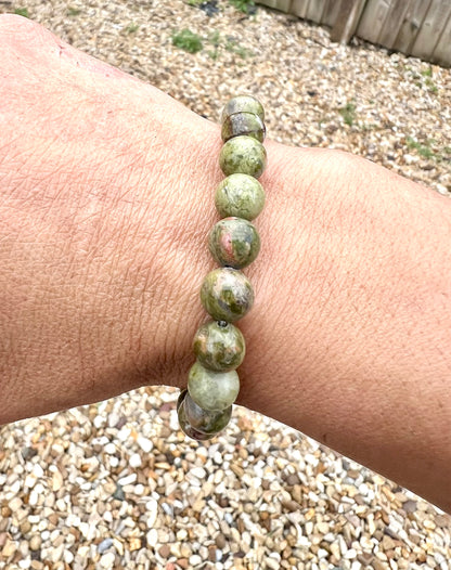 A hand wearing a bracelet composed of 8mm round green Unakite crystal gemstones.