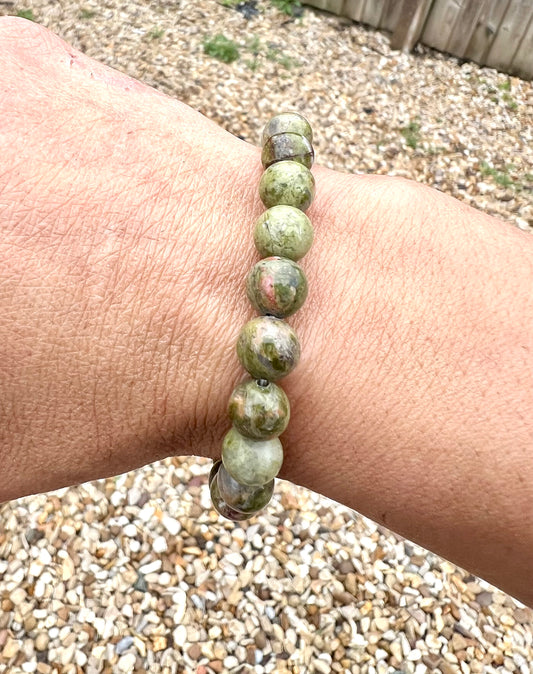 A hand wearing a bracelet composed of 8mm round green Unakite crystal gemstones.