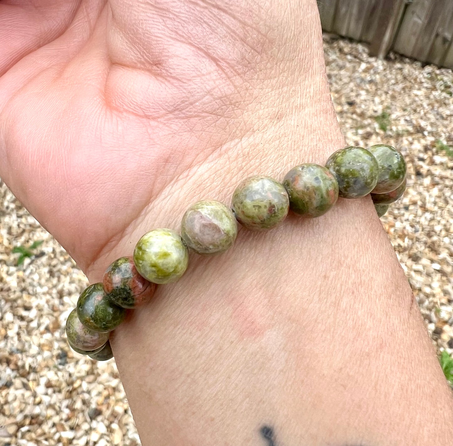 A hand wearing a bracelet composed of 8mm round green Unakite crystal gemstones.