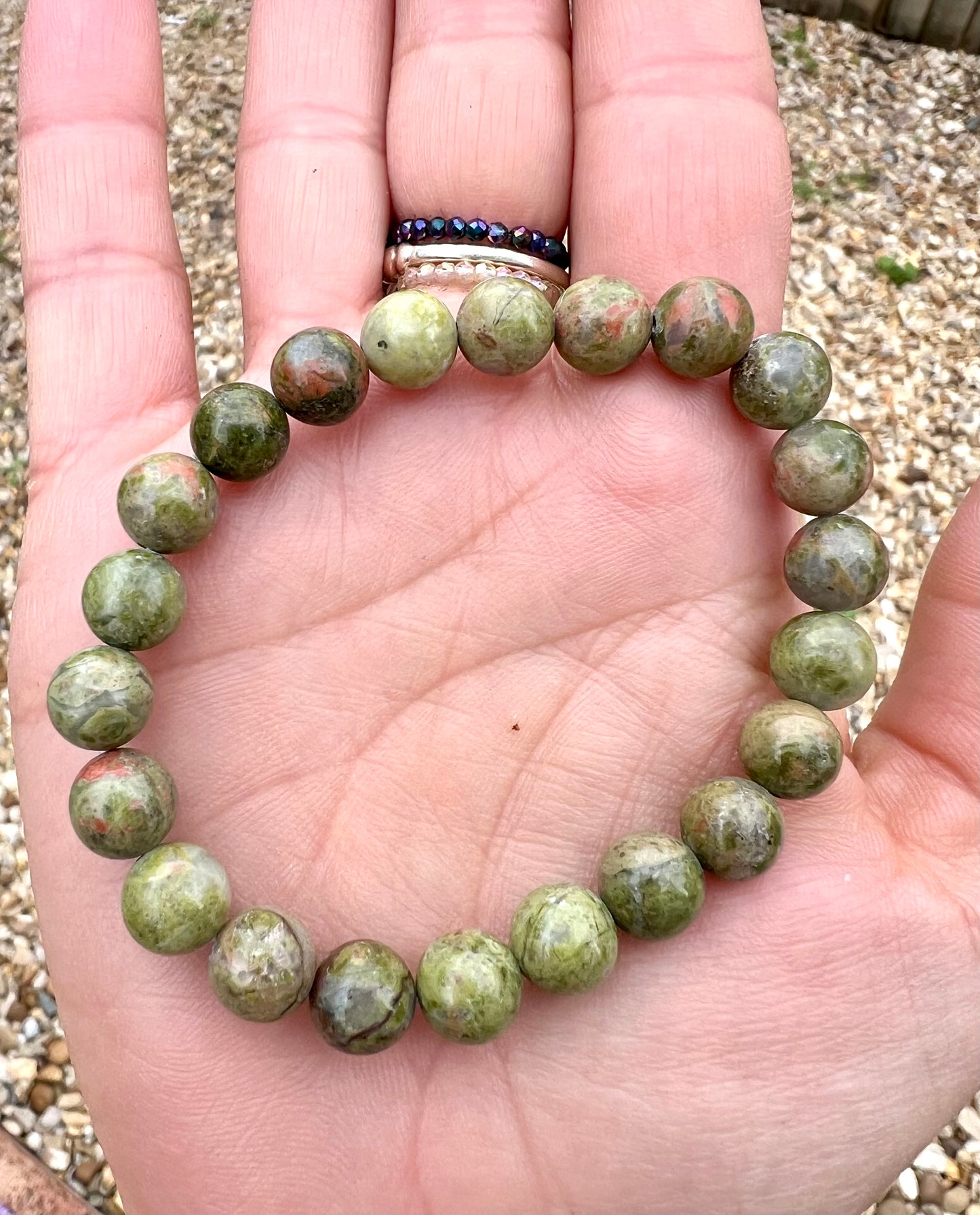 A hand holding a bracelet composed of 8mm round green Unakite crystal gemstones.