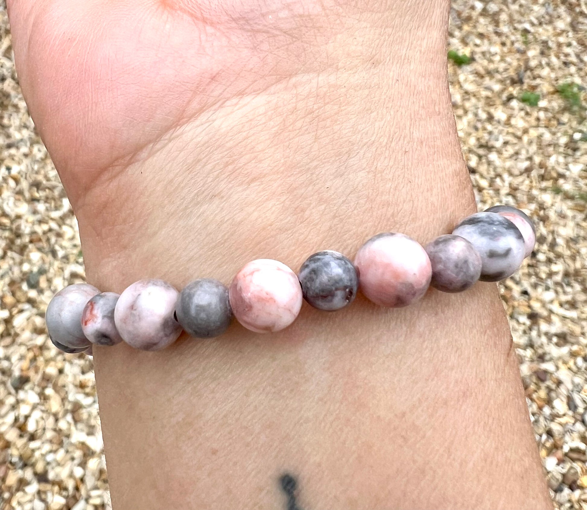 Beaded Zebra Jasper crystal bracelet on a wrist with a pebble background