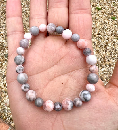 Beaded Zebra Jasper crystal bracelet in a hand with a pebble background
