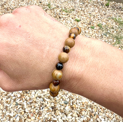 Hand wearing a beaded Wooden Jasper & tiger eye crystals bracelet with a pebbly surface behind