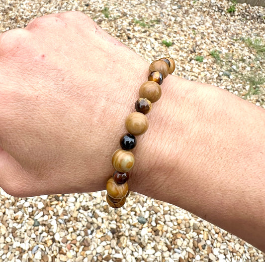 Hand wearing a beaded Wooden Jasper & tiger eye crystals bracelet with a pebbly surface behind