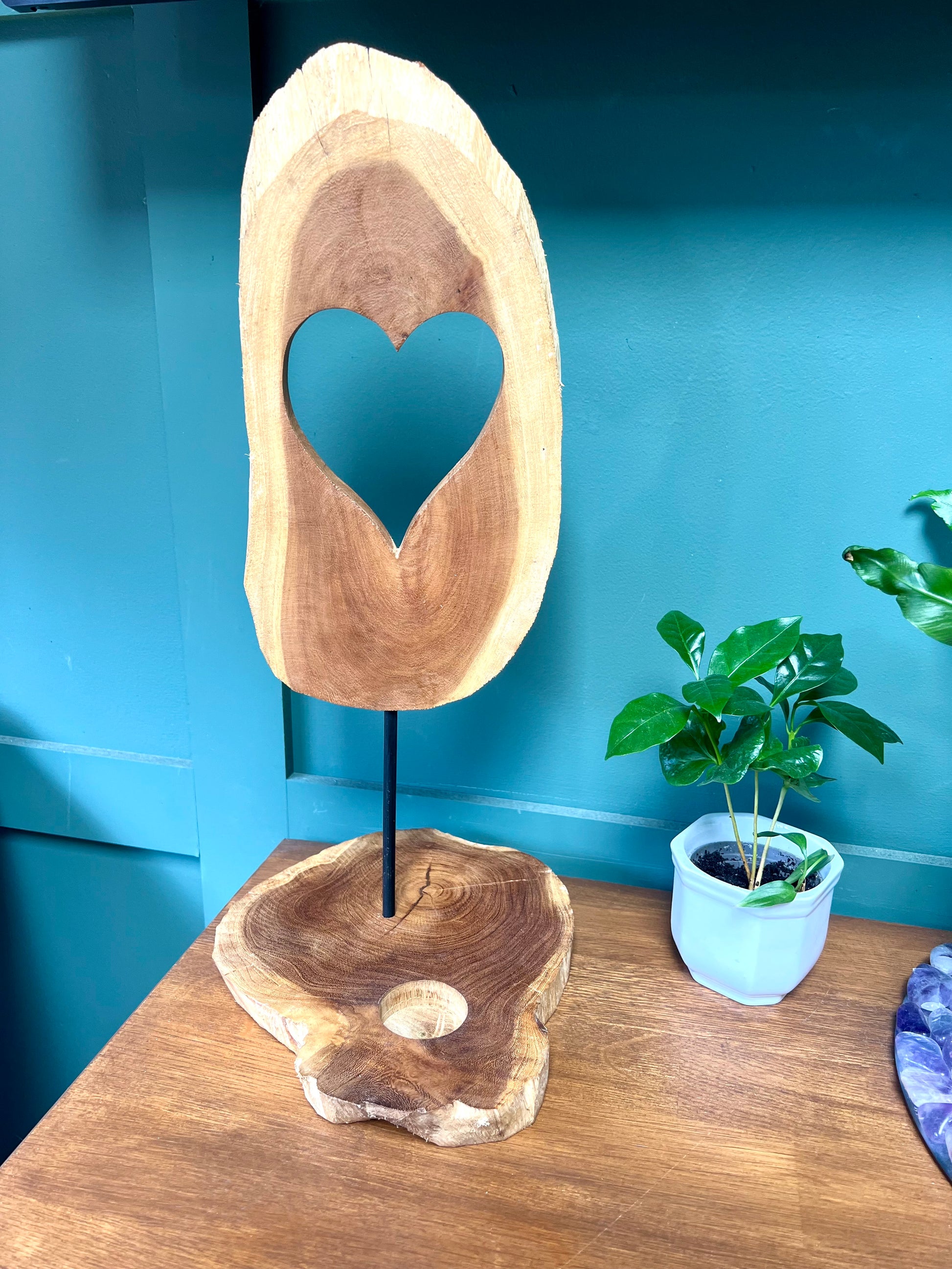 Wooden sculpture with a heart cutout on a stand against a blue wall.