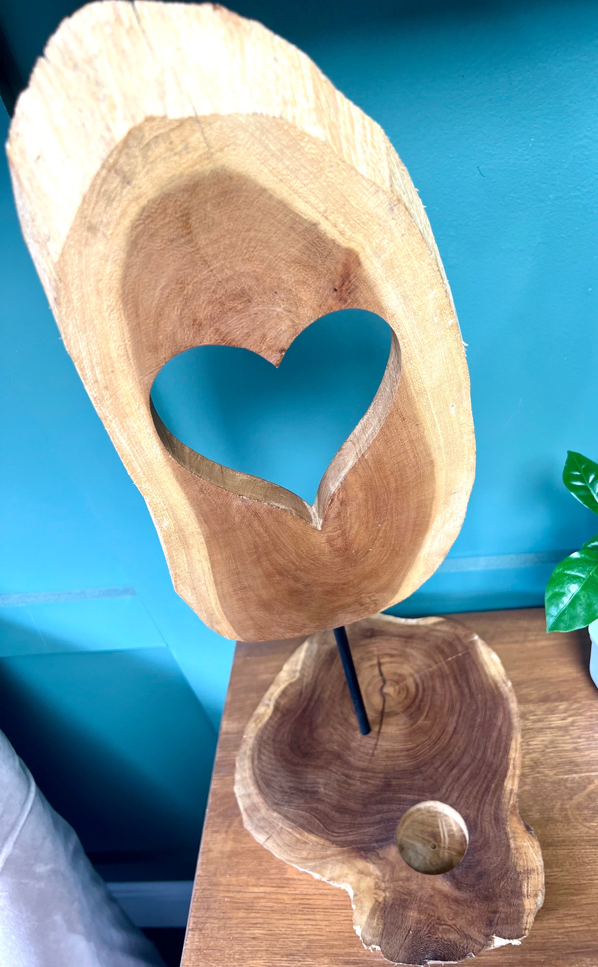 Wooden sculpture with a heart cutout on a stand against a blue wall.
