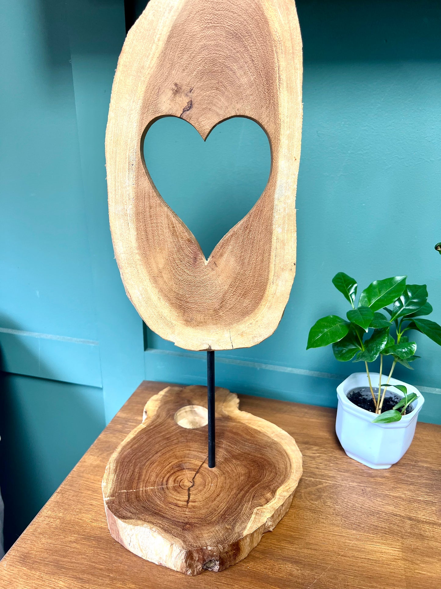 Wooden sculpture with a heart cutout on a stand against a blue wall.