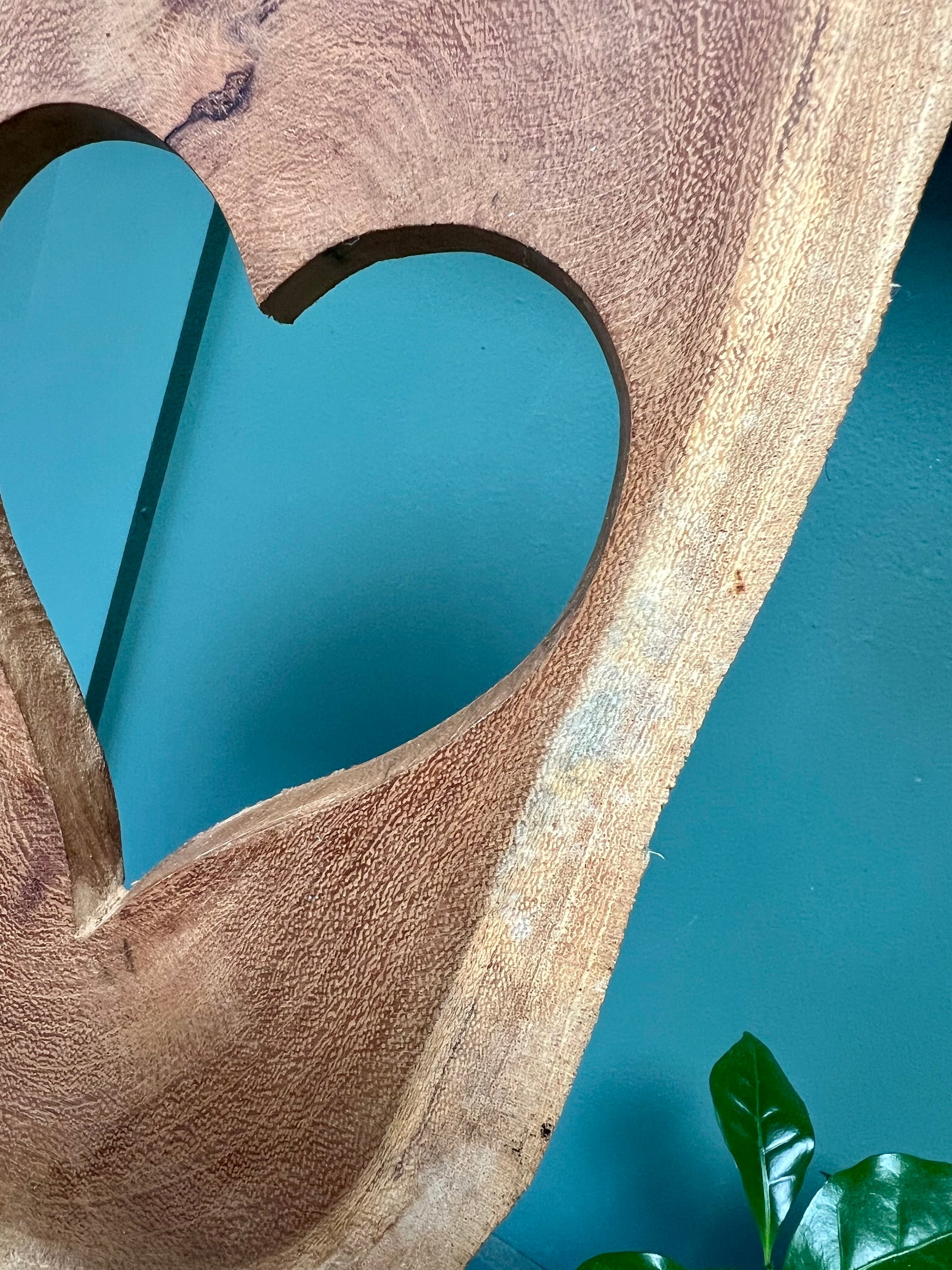Wooden sculpture with a heart cutout on a stand against a blue wall.