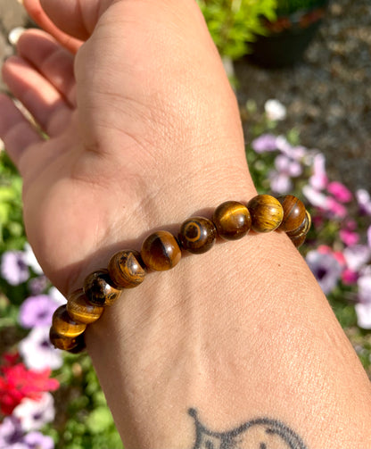 A hand wearing a bracelet composed of 8mm round golden-brown Tiger Eye crystal gemstones.
