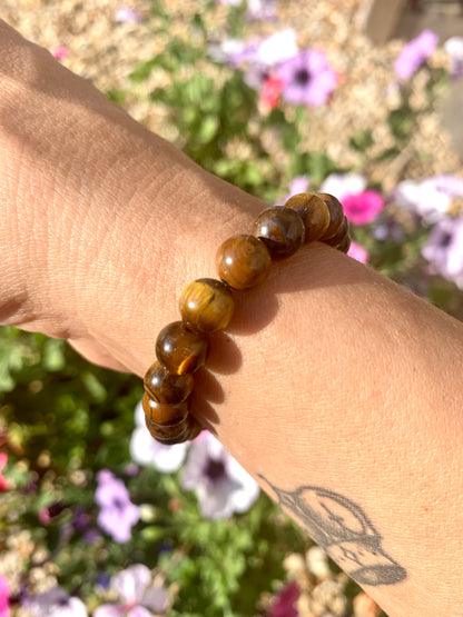 A hand wearing a bracelet composed of 8mm round golden-brown Tiger Eye crystal gemstones.