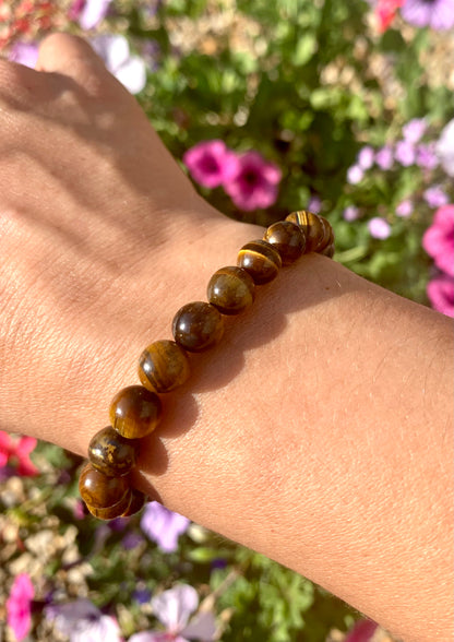 A hand wearing a bracelet composed of 8mm round golden-brown Tiger Eye crystal gemstones.